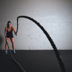 A focused woman performs a dynamic battle rope exercise in a gym setting, demonstrating strength and fitness.
